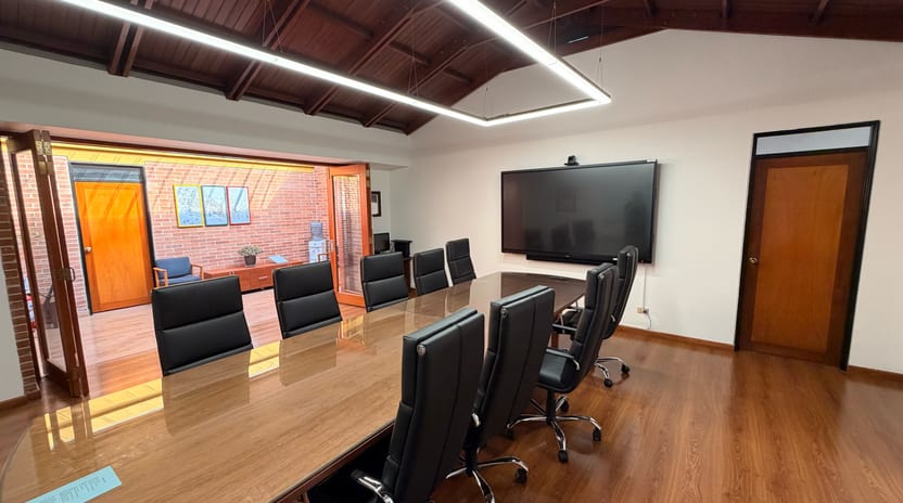 Sala de juntas con pantalla interactiva, cámara de videoconferencia encima y barra de sonido debajo